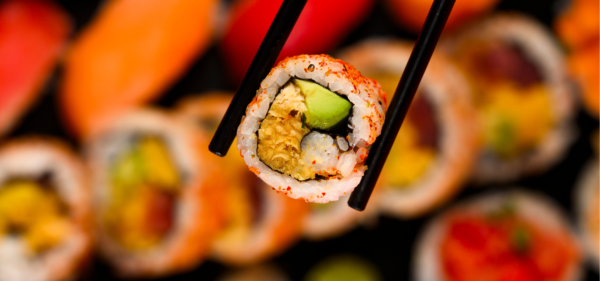 sushi tenu par des baguette noir au dessus d'un plateau de sushi